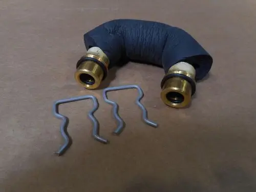 U-förmiges Anschlussstück mit zwei goldenen Metallanschlüssen und schwarzen Dichtungen, daneben zwei metallene Halterungen. Produkt von Remeha.